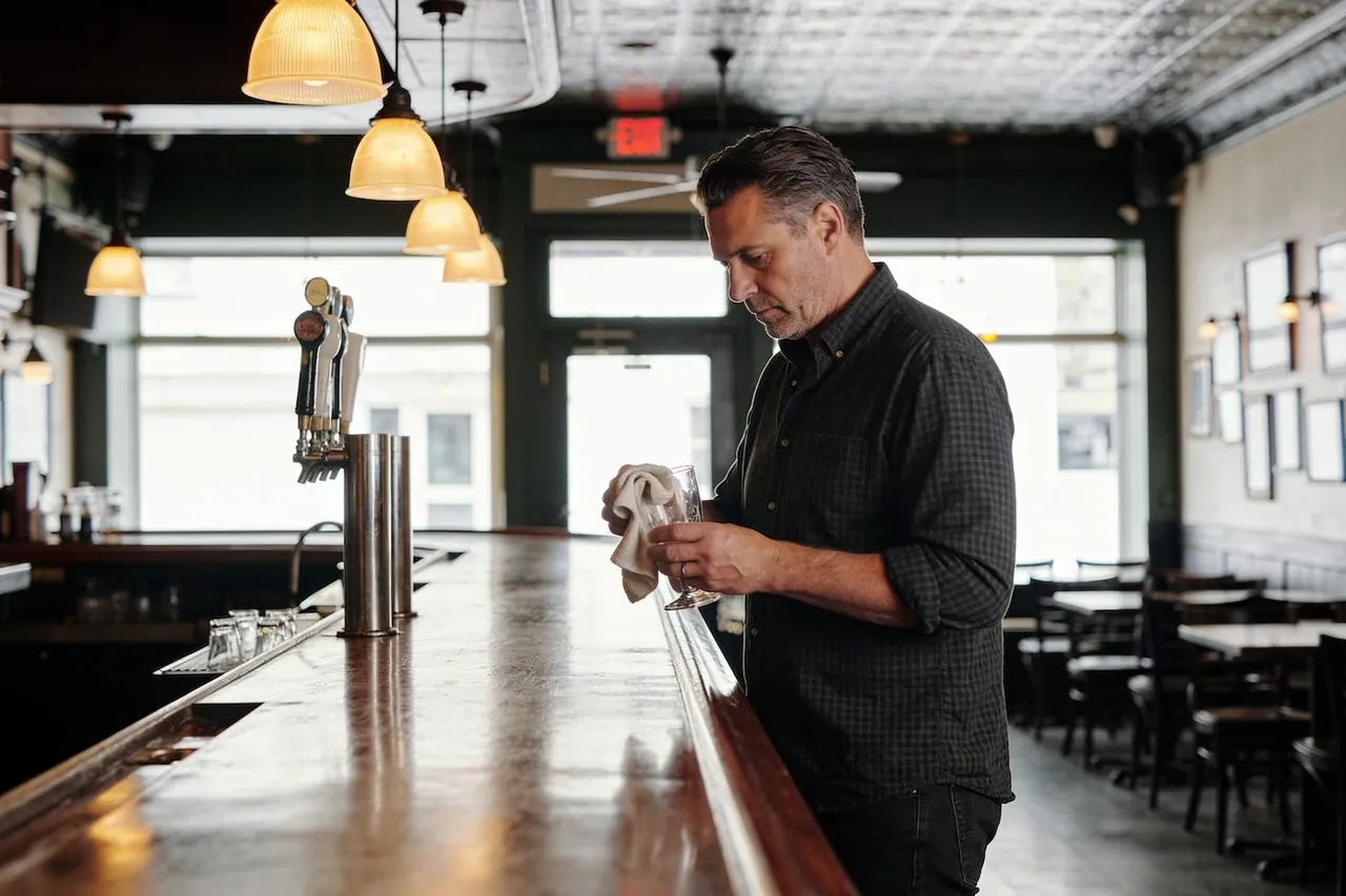 Bar owner polishing a glass behind the counter of their neighborhood bar