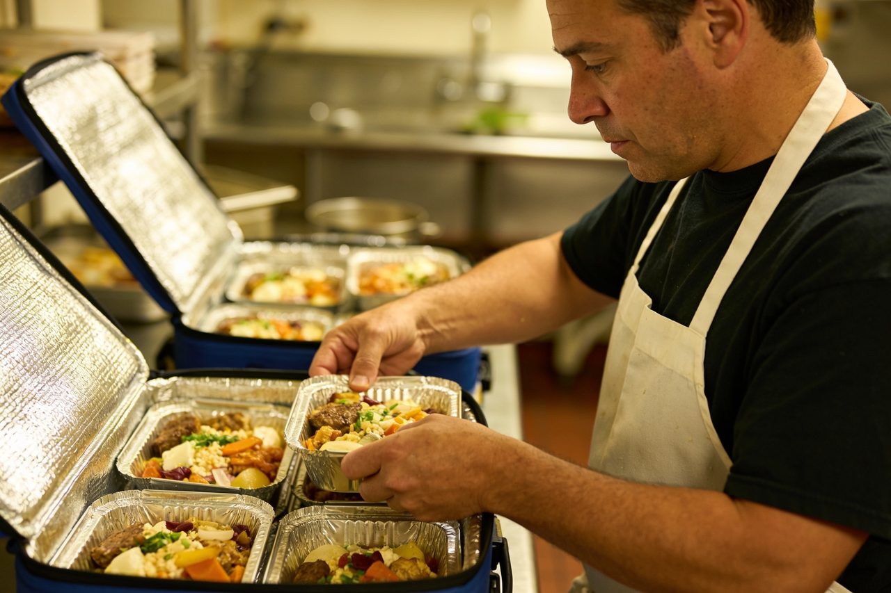 Catering owner packing prepared meal trays into insulated carriers in a commercial kitchen - catering business funding