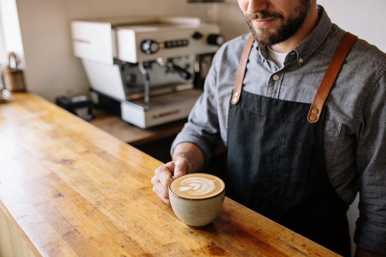 Coffee shop owner setting a fresh latte on the counter of their cafe - coffee shop business funding