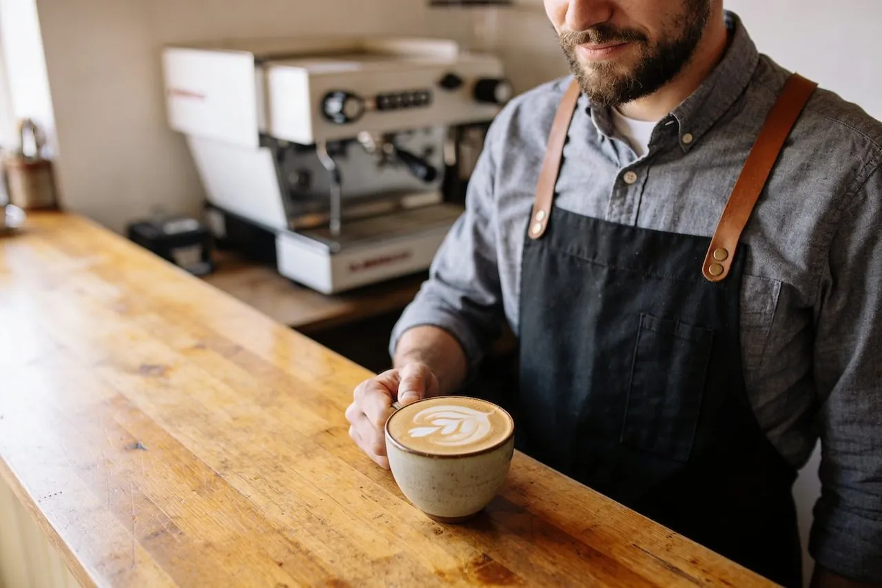 Coffee shop owner setting a fresh latte on the counter of their cafe