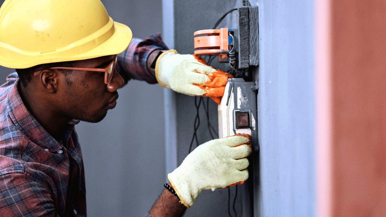 Electrician in a hard hat working on a wall-mounted electrical box