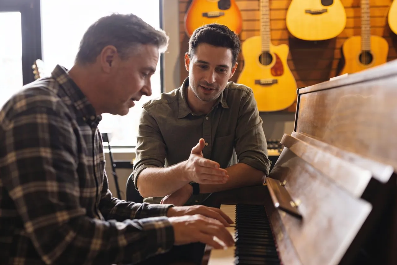 Music school owner giving a piano lesson beside a wall of guitars