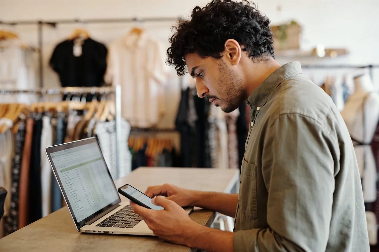 Boutique owner reviewing business finances on a laptop and phone at the counter