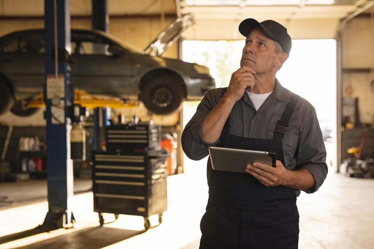 Auto repair shop owner holding a tablet in his garage bay while planning ahead