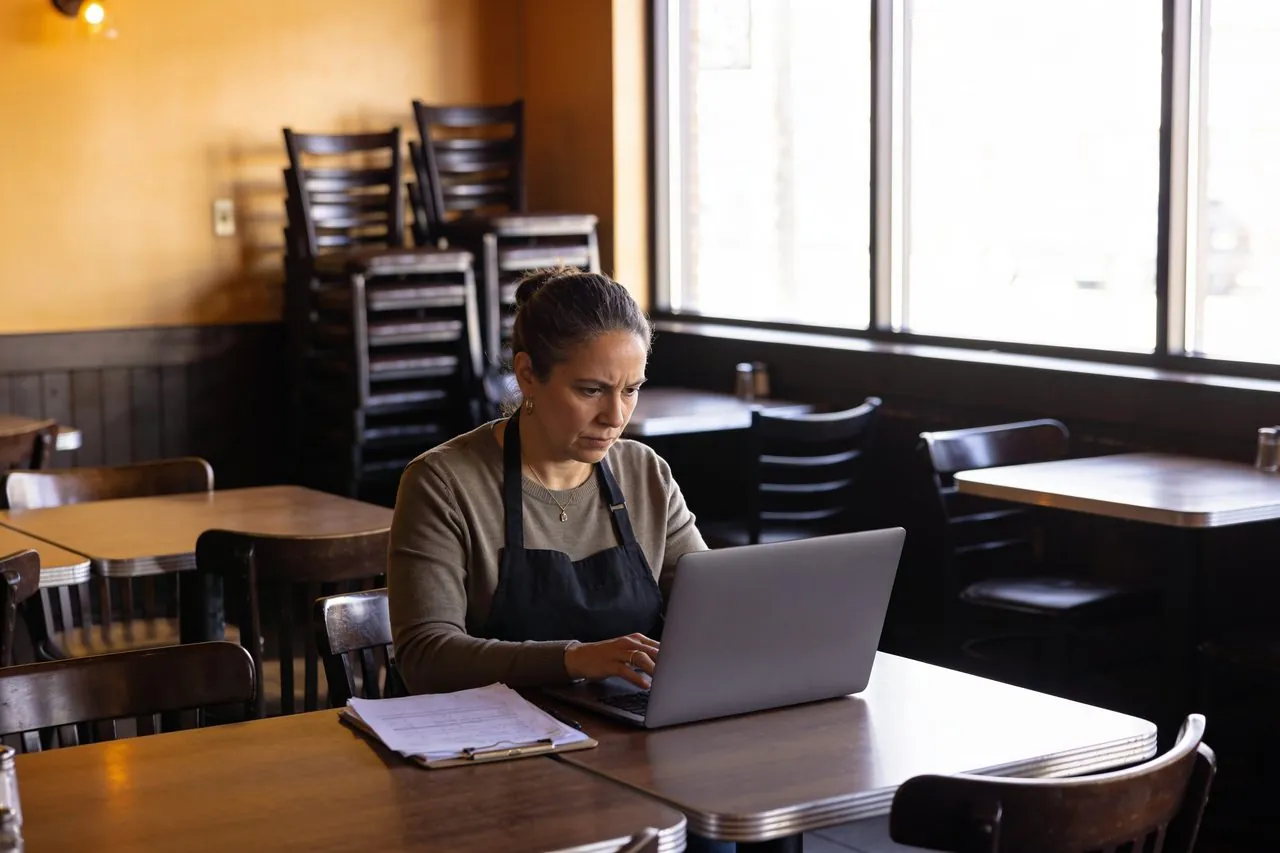 Restaurant owner reviewing her finances on a laptop in the empty dining room