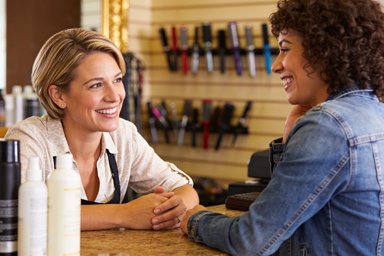 Salon owner talking with a happy customer at the front counter to gauge customer satisfaction.