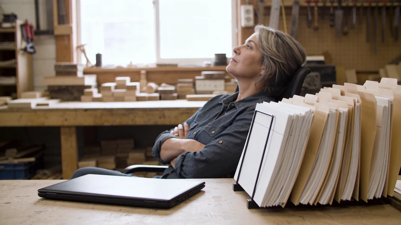 Small business owner sitting back from her desk in a workshop office, thinking through her funding options