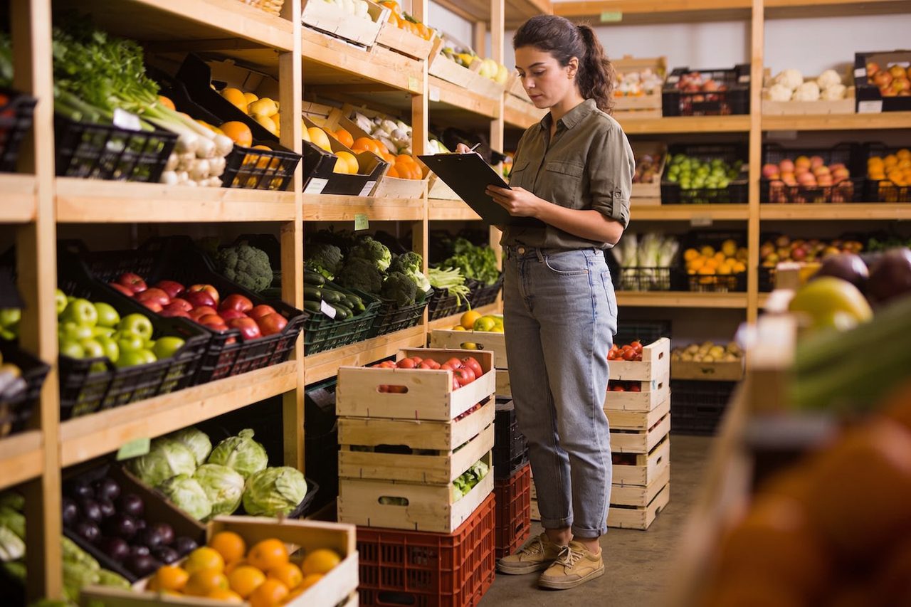 Grocery market owner checking inventory beside stocked produce shelves