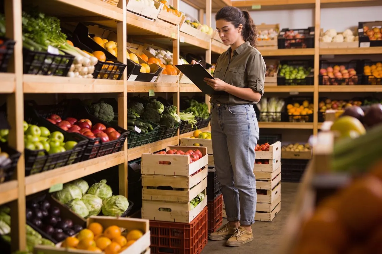 Grocery market owner checking inventory beside stocked produce shelves