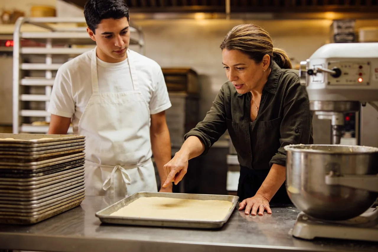 Bakery owner walking an employee through a prep process